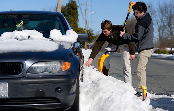 Hunter Allred and Abdel Asmar work to free a car stuck by snow banks on Briarcliff Road in Burlington Friday.