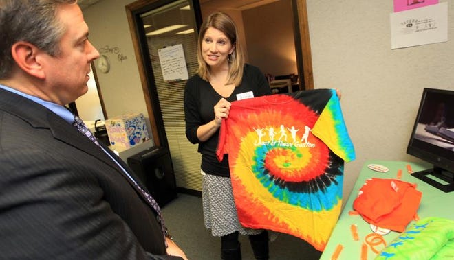 CaroMont CEO Doug Luckett, left, checks out ‘Least of These Gaston’ shirts shown by ‘Least of These’ executive director Susanna Kavanaugh during an open house Thursday at the foster care advocacy group’s new location on Remount Road.