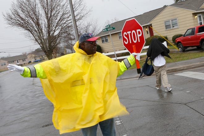 Walter Marshall, crossing guard, holds traffic for a young student at Onslow Drive and New River Drive intersection on a windy and rainy afternoon.