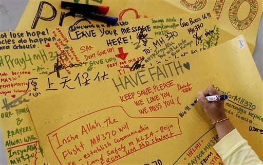 A woman writes a wishing message on a cardboard at Kuala Lumpur International Airport in Sepang, Malaysia, Monday, March 10, 2014. Vietnamese aircraft spotted what they suspected was one of the doors of the missing Boeing 777 on Sunday, while questions emerged about how two passengers managed to board the ill-fated aircraft using stolen passports.