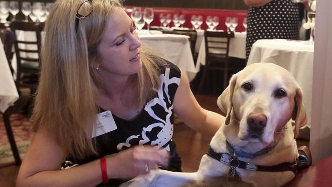 Wine specialist Amy Dixon holds the paw of her beloved guide dog Elvis just prior to the the start of a wine tasting event at Pistache French Bistro on Clematis St., March 4, 2014. Dixon, who travels the nation to raise awareness for Guiding Eyes for the Blind - the nonprofit, New York-based school that trained Elvis - lost 97 percent of her sight due to a rare inflammatory eye disease. (Damon Higgins / The Palm Beach Post)