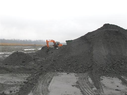 An excavator works beside a mound of ash at the pond at Santee Cooper's Jefferies power generating station just outside Moncks Corner, S.C., on Feb. 26, 2014. The recycled coal ash is trucked from the site and then used in the manufacture of concrete. Santee Cooper is South Carolina's state-owned electric and water utility. (AP Photo/Bruce Smith)