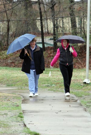 JAMIE MITCHELL • TIMES RECORD / Jo Ward, left, and Lisa Hammersly use their umbrellas to block the cold rain Sunday, March 16, 2014, as they make their way around the Creekmore Park walking path.