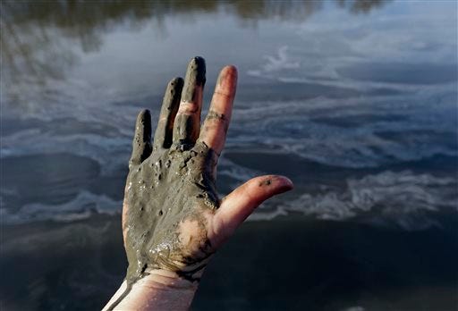 FILE - In this Feb. 5, 2014 file photo, Amy Adams, North Carolina campaign coordinator with Appalachian Voices, shows her hand covered with wet coal ash from the Dan River swirling in the background as state and federal environmental officials continued their investigations of a spill of coal ash into the river in Danville, Va. A federal grand jury is convening Tuesday, March 18, 2014, as part of a widening criminal investigation triggered by the massive Duke Energy coal ash spill that coated 70 miles of the Dan River with toxic sludge. (AP Photo/Gerry Broome, File)
