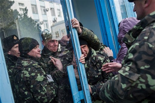 Pro-Russian self-defense force members get through an entrance to the Ukrainian Navy headquarters in Sevastopol, Crimea, Wednesday, March 19, 2014. An Associated Press photographer said several hundred militiamen took down the gate and made their way onto the base. They then raised the Russian flag in the square by the headquarters. The unarmed militia waited for an hour on the square before the move to storm the headquarters. Following the arrival of the commander of the Russian Black Sea fleet, the Crimeans took over the building.