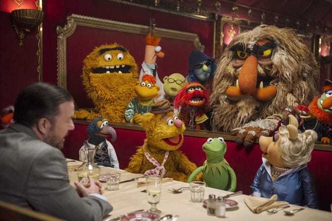 Ricky Gervais, left, as the villainous Dominic Badguy, dines with Gonzo, Fozzie the Bear, Kermit, Miss Piggy and the Muppet gang in “Muppets Most Wanted.”