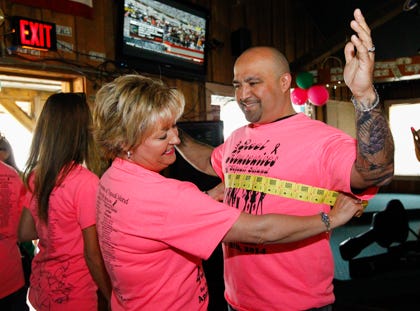 Annete Erny, event organizer, measures Dwight Torres, owner of Topsail Barber shop and a sponsor of the event, for tickets that support the 26-mile Island Bike ride.