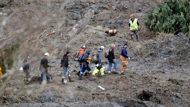 Searchers walk into the scene of a deadly mudslide that covers the road, Wednesday, March 26, 2014, in Oso, Wash. Sixteen bodies have been recovered, but authorities believe at least 24 people were killed. And scores of others are still unaccounted for, although many of those names were believed to be duplicates or people who escaped safely. (AP Photo/Rick Wilking, Pool)