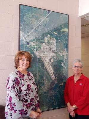 Paula Adams and Kathy Noel pose with an aerial photo of the Chippewa County International Airport and the Industrial Park having spent more than 30 years apiece promoting economic development in our area. Both women said they plan to spend more time with their grandchildren after leaving the EDC for the final time on Friday.