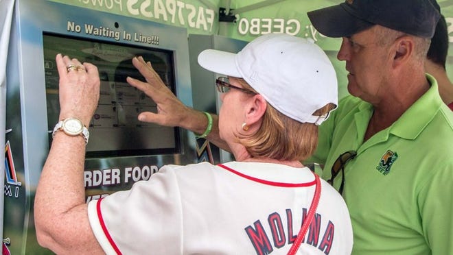 Karen Sailor, from St. Louis, is helped by Joseph Parsons, sales representative for JCS Enterprises, as she makes a food purchase at Roger Dean Stadium in Jupiter. The Virtual Concierge kiosks in use at Roger Dean Stadium were manufactured by JCS Enterprises.