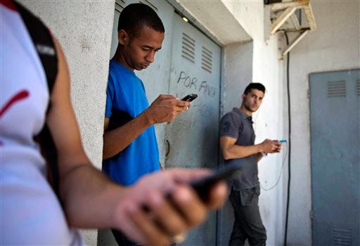 Students gather behind a business looking for a Internet signal for their smart phones in Havana, Cuba, Tuesday, April 1, 2014. The U.S. Agency for International Development masterminded the creation of a "Cuban Twitter," a communications network designed to undermine the communist government in Cuba, built with secret shell companies and financed through foreign banks, The Associated Press has learned. The project, which lasted more than two years and drew tens of thousands of subscribers, sought to evade Cuba's stranglehold on the Internet with a primitive social media platform. Its users were neither aware it was created by a U.S. agency with ties to the State Department, nor that American contractors were gathering personal data about them. In 2012, the text messaging service vanished as mysteriously as it appeared. (AP Photo/Ramon Espinosa)