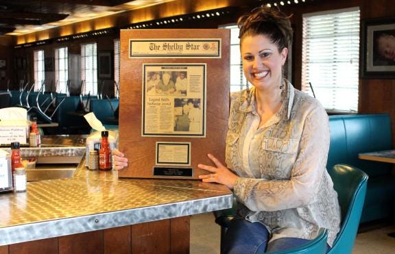 Natalie Ramsey, VP of Red Bridges Barbecue, remembers when Mickey Rooney visited the restaurant in 1997. She holds a Shelby Star article that hangs in the restaurant.