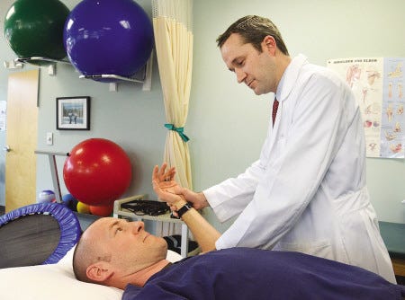 Dr. David Davis, an orthopaedic surgeon at Access Sports Medicine and Orthopaedics with an office in Portsmouth, demonstrates checking the shoulder for injury to the acromioclavicular (AC) joint on Kevin Strachan, an athletic trainer and cast technician at Access Sports.