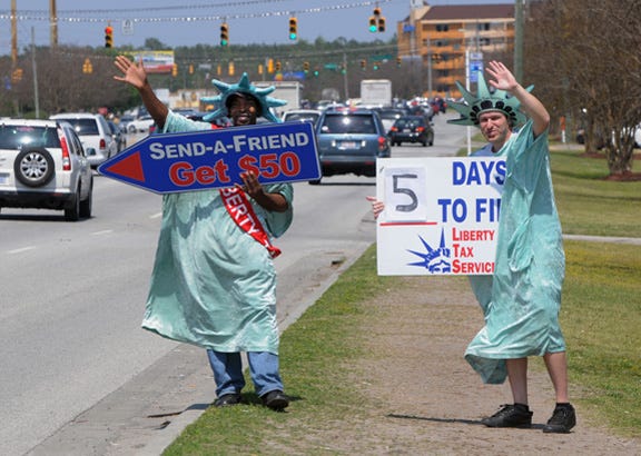 Edmond Hodge, left, and Wayne Goodman, wearing Statue of Liberty suits, hold signs advertising Liberty Tax Service at University Landing on South College Road in Wilmington on April 10.