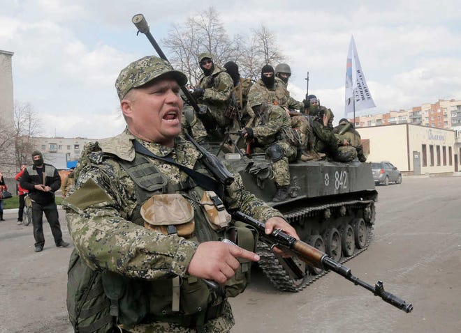 A pro-Russian gunman clears the way for a combat vehicle with gunmen on top in Slovyansk, Ukraine, Wednesday, April 16, 2014. The troops on those vehicles wore green camouflage uniforms, had automatic weapons and grenade launchers. At least one had the St. George ribbon attached to his uniform, which has become a symbol of the pro-Russian insurgency in eastern Ukraine. (AP Photo/Efrem Lukatsky)