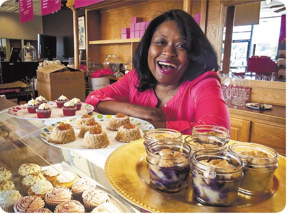 Nicole Sullivan and her business, Sweet Boutique Bakery in Belk at Cross Creek Mall, will be making a selection of sweets for the U.S. Open. The three treats in front of her are some of the sweets planned. From left they are red velvet cupcakes, Arnold Palmer Southern Pound Cake and blueberry-peach Mason jar cobbler.