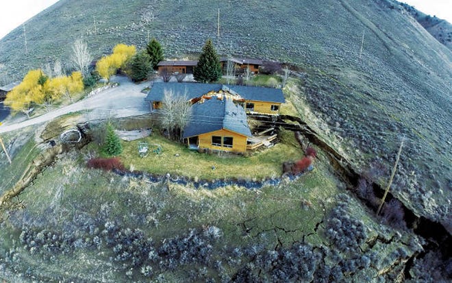 This aerial image provided by Tributary Environmental shows a home damaged by a landslide Friday, April 18, 2014 in Jackson, Wyo. A slow-moving landslide in Jackson sped up significantly Friday, splitting this house in two, causing a huge uplift in a road and a Walgreens parking lot, and threatening to destroy several other unoccupied homes and businesses. (AP Photo/Tributary Environmental) NO SALES