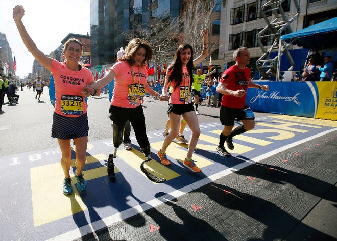 Double amputee Celeste Corcoran, center, a victim of last year's bombings, reaches the finish line of the 118th Boston Marathon, Monday, April 21, 2014, in Boston, with the aid her sister Carmen Acabbo, left, and daughter Sydney, right, who was also wounded last year.