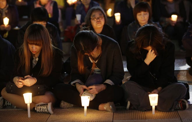 A woman wipes tears during candlelight vigil for safe return of passengers of the sunken ferry Sewol in Ansan, South Korea, Friday, April 25, 2014. As visiting President Barack Obama offered South Koreans his condolences Friday for the ferry disaster, the South Korean government conceded that some bodies have been misidentified and announced changes to prevent such mistakes from happening again.