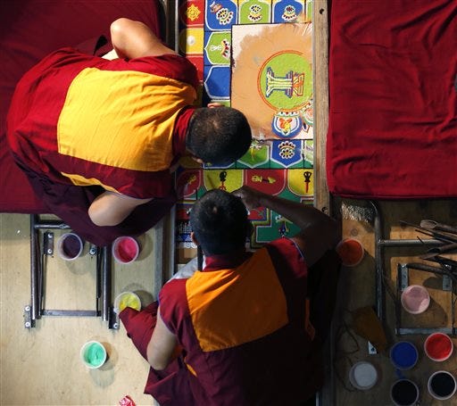Buddhist monks work on fixing a sand mandala, which was disturbed by a small child at Jersey City City Hall, Friday, April 25, 2014, in Jersey City, N.J. The monks have been building the sand mandala since Monday. It's a traditional, multicolored display that is built then destroyed in a ceremony meant to symbolize the fleeting nature of life. The young child climbed over a rope barrier and got onto the four-foot-square display. The sides and middle were smudged as a result.