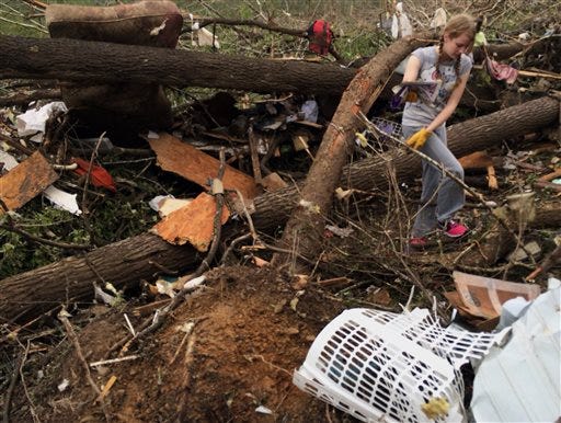 In this Monday, April 28, 2014, photo taken with a cell phone, Emily Tittle picks through rubble after a tornado stuck Sunday, in Paron, Ark. Tittle said she, her eight siblings and her parents went for safety under the stairs in the two-story house, but only half of them made it before the walls were obliterated by the twister that left just the foundation behind. Her father, Rob Tittle, and two sisters, Tori, 20, and Rebekah, 14, were killed in the storm. (AP Photo/Christina Huynh)