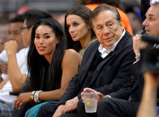 In this file photo taken on Friday, Oct. 25, 2013, Los Angeles Clippers owner Donald Sterling, right, and V. Stiviano, left, watch the Clippers play the Sacramento Kings during the first half of an NBA basketball game in Los Angeles. Used car dealership chain CarMax says it is ending its sponsorship of the Clippers in the wake of racist comments attributed to Sterling. (AP Photo/Mark J. Terrill, File)