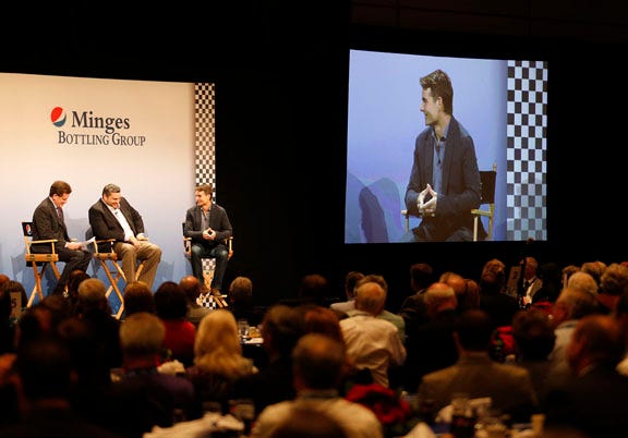 Al Carey, PepsiCo CEO, left, and Lou Arbetter, director of brand marketing, center, interview NASCAR driver Jeff Gordon, at right and projected on the screen, in front of an enthusiastic crowd.