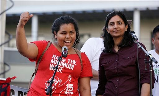 File -- In this May 1, 2014 file photo, Seattle City Council Member Kshama Sawant, right, looks on as Stephanie Sucasaca holds up a fist as Sawant had just done while interpreting Sawant's remarks into Spanish at a May Day rally in support of immigrant and workers rights and a boost in the minimum wage, in Seattle. While the Seattle mayor is proposing to raise the wage to $15 in the coming years to the highest level in the nation, some activists say that's too slow and are threatening to take the issue to voters with a ballot measure that would force a raise sooner. (AP Photo/Elaine Thompson, File)