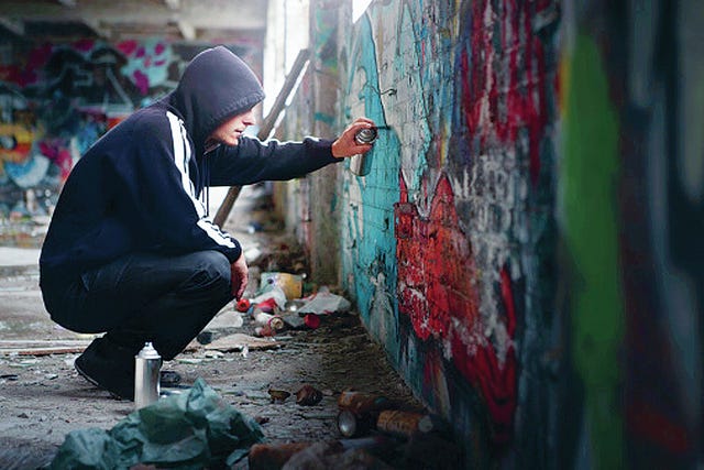Illegal Young man Spraying paint on a Graffiti wall.