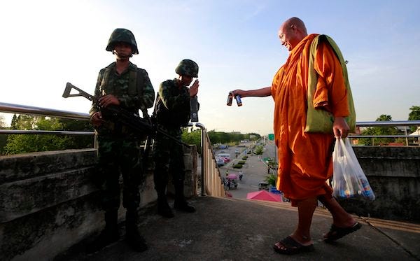 A Buddhist monk offers energy drinks to Thai soldiers guarding a pedestrian overfly near the site where pro-government demonstrators stage a rally on the outskirts of Bangkok, Thailand Tuesday, May 20, 2014. Thailand's powerful army declared martial law Tuesday and deployed troops into the heart of Bangkok in a dramatic move it said was aimed at stabilizing the Southeast Asian country after six months of turbulent political unrest. The military insisted a coup d'etat was not underway. THE ASSOCIATED PRESS