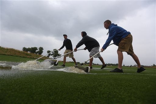 Grounds crew members CJ Watson, Trey Bishop and Payton Neufeld roll water to a drain on the first fairway during a rain delay in the first round of the NCAA men's golf championship Friday, May 23, 2014, at Prairie Dunes Country Club in Hutchinson, Kan.