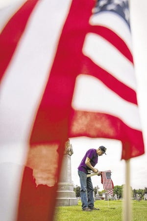 Danny DaSilva, of the Cape Verdean American Veterans Association, places flags Friday on the gravesites of veterans at St. John Cemetery on Allen Street in New Bedford.