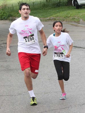 Adrian Figueroa, 19, holds hands with his running buddy Laurel Padilla, 11, as they near the finish line Saturday of the eighth Girls on the Run 5-kilometer race on the east side of the YWCA in the 1200 block of S.W. Jackson. About 480 people took part in the race.