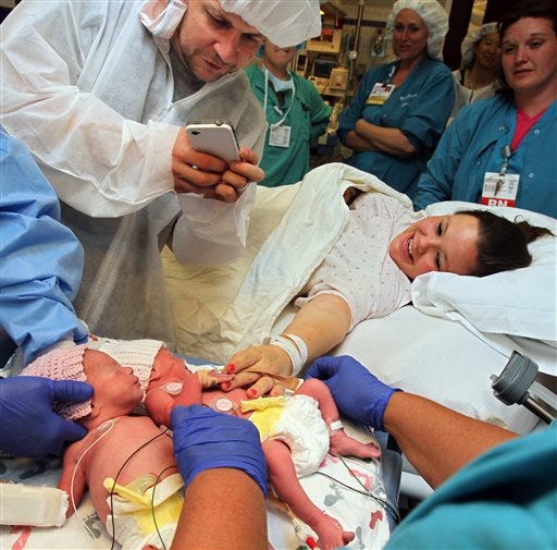 In this May 9, 2014 photo, Sarah Thistlethwaite, right, touches her twin daughters, Jillian, center, and Jenna, for the first time while her husband, Bill, snaps photos after her delivery of the monoamniotic twin girls at Akron General Hospital in Akron, Ohio. The identical twin girls shared the same amniotic sac and placenta, which doctors say occurs in about one of every 10,000 pregnancies.