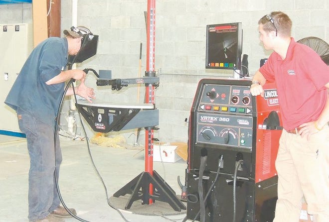 A visitor to the Industrial Arts Institute’s open house last week in Onaway tries his skills on a Virtual Reality Arc welding simulator. Below, attendees are seen in one of the classrooms reading graphic, instructional material pertaining to welding and fabricating processes.