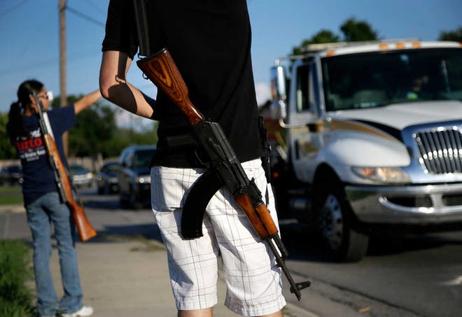 FILE - In this May 29, 2014, file photo, Kory Watkins, front, coordinator for Open Carry Tarrant County, carries his Romanian AK 47 over his shoulder as he and his wife Janie, rear, along with others, gather for a demonstration in Haltom City, Texas. Companies, customers and others critical of Texas gun rights advocates who have brought military-style assault rifles into businesses as part of demonstrations supporting "open carry" gun rights now have a surprising ally: the National Rifle Association. The NRA has long been a zealous advocate for gun owners' rights. But the group's lobbying arm, the Institute for Legislative Action, has called the demonstrations counterproductive to promoting gun rights, scary and "downright weird." (AP Photo/Tony Gutierrez, File)
