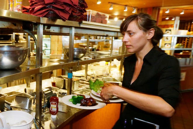 In this June 2, 2014 photo, Wendy Harrison, a waitress at the icon Grill in Seattle, picks up a food order from the kitchen as she works during lunchtime. An Associated Press comparison of the cost of living at several other major U.S. cities found that a $15 minimum wage, like Seattle adopted this week, will make a difference, but won't buy a lavish lifestyle. (AP Photo/Ted S. Warren)