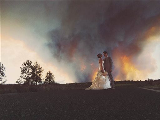 In this Saturday, June 7, 2014 photo provided by Josh Newton, newlyweds Michael Wolber and April Hartley pose for a picture near Bend, Ore., as a wildfire burns in the background. Because of the approaching fire, the minister conducted an abbreviated ceremony and the wedding party was evacuated to a downtown Bend park for the reception.