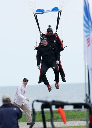 Former President George H.W. Bush, strapped to Sgt. 1st Class Mike Elliott, a retired member of the Army's Golden Knights parachute team, prepare to land on the lawn at St. Anne's Episcopal Church while celebrating Bush's 90th birthday in Kennebunkport, Maine, Thursday, June 12, 2014. (AP Photo/Robert F. Bukaty)