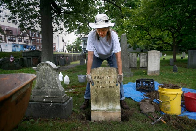 TaMara Conde has been hired by the City of Quincy to restore crumbling and toppled gravestones in the city’s historic Hancock Cemetery next to city hall. Above, Conde sets a cleaned marble stone back in place after removing rocks from the hole and putting in a new bed of gravel.