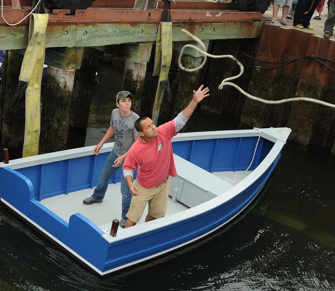 Pirate Cove East yard manager Steven Perry reaches out to catch a line as he and Tiverton High sophomore Alec Figueiredo man the flat-decked, flat-bottomed work skiff built by high school students.