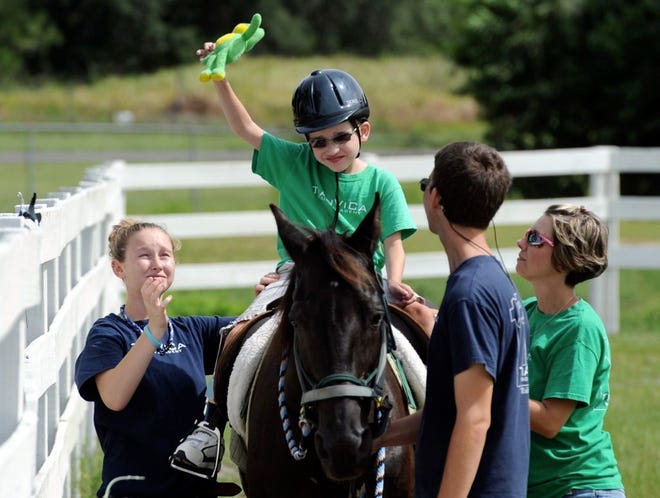 Devlin York, 7, gets a stuffed frog off the fence with help from side rider, Lauren Branam, left, while participating in therapeutic lessons at TiAnViCa Riding Academy in Bartow. At right is his mom, Amy York, and side rider Nathan Calhoun.