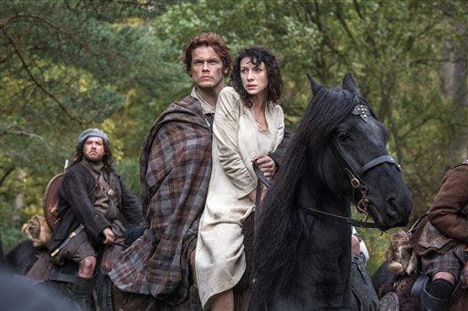 This image released by Starz shows Sam Heughan, center left, and Caitriona Balfe in a scene from "Outlander," premiering Aug. 9 on Starz. Balfe portrays Claire Randall, a married combat nurse in 1945 who is swept back to 18th-century Scotland, where she meets a dashing warrior she is compelled to wed.