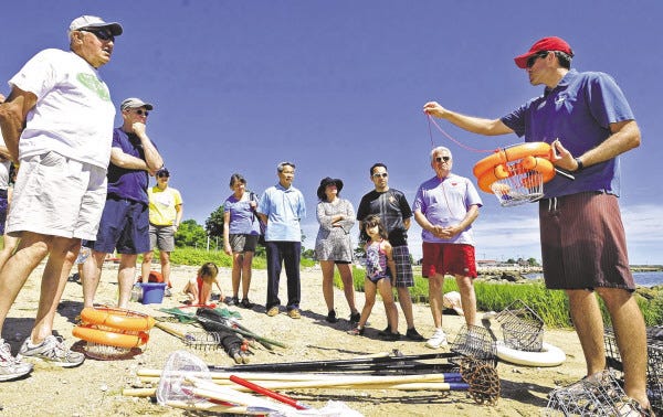 Rob Hancock, far right, from the Buzzards Bay Coalition demonstrates a peck basket during a class to teach the basics of quahogging on Saturday at Fort Taber Park in the South End of New Bedford.