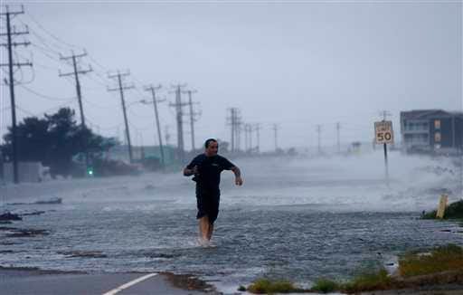 A man crosses a flooded Highway 64 as wind pushes water over the road as Hurricane Arthur passes through Nags Head, N.C., Friday.