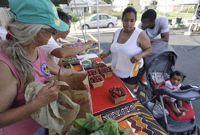 Peace By Piece farm owners, from left, Judy Dauson, 66, and Cyndy Beck, 55, help customer Danielle Johnson purchase produce at a farmer's market near St. Paul Church in Erie on June 30. With Johnson, 25, are Ian Stewart, 24, and her daughter Nariah Johnson, seven months old.  JACK HANRAHAN/