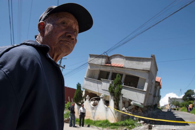 A man stands close to homes that collapsed during an earthquake in San Pedro, Guatemala, Monday, July 7, 2014. A magnitude-6.9 earthquake on the Pacific Coast jolted a wide area of southern Mexico and Central America Monday.