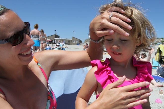 Meghan Wood, of Warwick, rubs sunscreen on daughter Marielle's face during their recent visit to the beach.