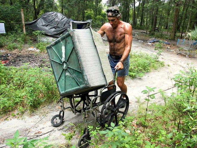 Vincent Charo, known in the Tent City community as "Uncle Vinnie," wheels a doghouse on an old wheelchair from an abandoned campsite at Tent City on Sunday.