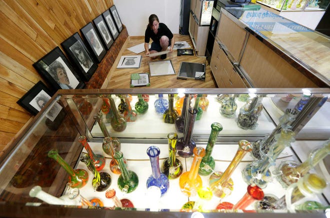 Krystal Klacsan prepares artwork to be hung, Monday, July 7, 2014 behind a case displaying glass bongs at the recreational marijuana store Cannabis City in Seattle. When legal sales begin on Tuesday, July 8, 2014, the store will be the first and only store in Seattle to initially sell recreational marijuana. (AP Photo/Ted S. Warren)